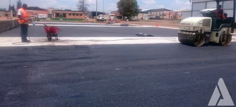 Trabajador y rodillo tándem compactando la carpeta asfáltica de un patio industrial