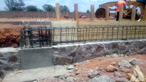 Castillos de varilla y cimbra de madera sobre muro de mampostería con motoconformadora al fondo