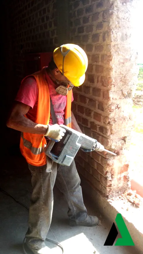 Trabajador con casco y rotomartillo demoliendo un muro de ladrillo durante una remodelación