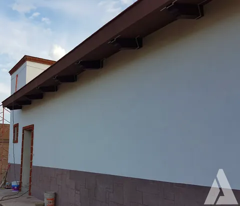 Fachada remodelada con muro liso, zoclo de piedra y pérgola de perfiles metálicos en el alero