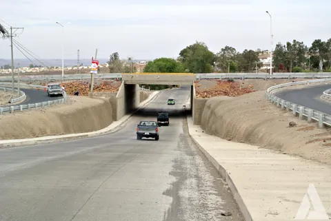 Vehículos circulando por un paso a desnivel de concreto recién construido con taludes revestidos