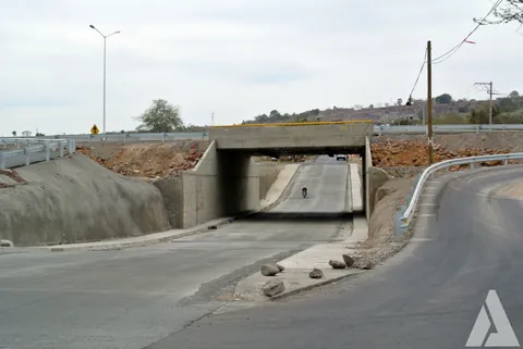 Vista frontal de un paso a desnivel de concreto con puente superior y barreras metálicas laterales
