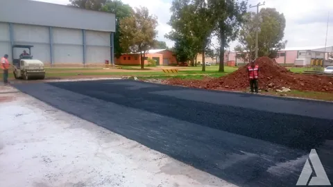Rodillo compactador trabajando sobre carpeta asfáltica nueva en un patio junto a una nave