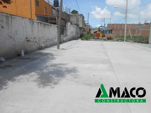 Calle pavimentada con losas de concreto hidráulico y máquina de trabajo al fondo