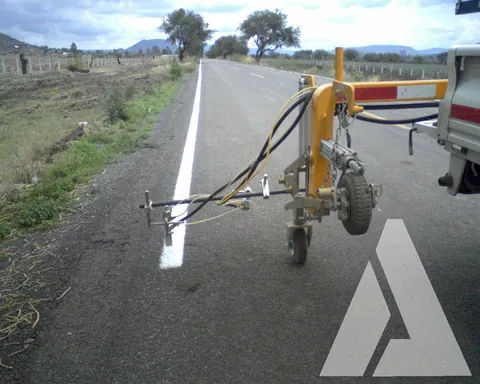 Equipo pintarrayas aplicando la raya lateral blanca sobre el acotamiento de una carretera