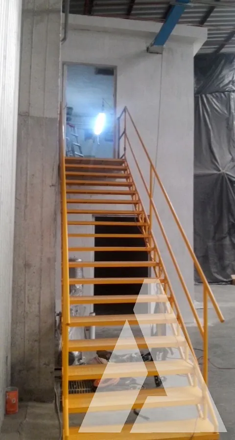 Escalera metálica industrial pintada de amarillo con barandal, fabricada e instalada en el interior de una nave