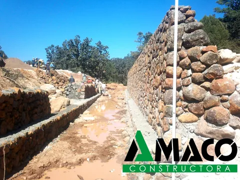 Canal hidráulico con muros de mampostería de piedra en construcción, con cuadrilla trabajando al fondo