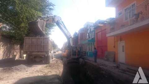 Excavadora descargando material en un camión de volteo sobre la zanja del colector de drenaje