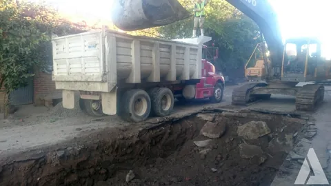 Excavadora cargando un camión de volteo durante la apertura de una zanja de drenaje en una calle urbana